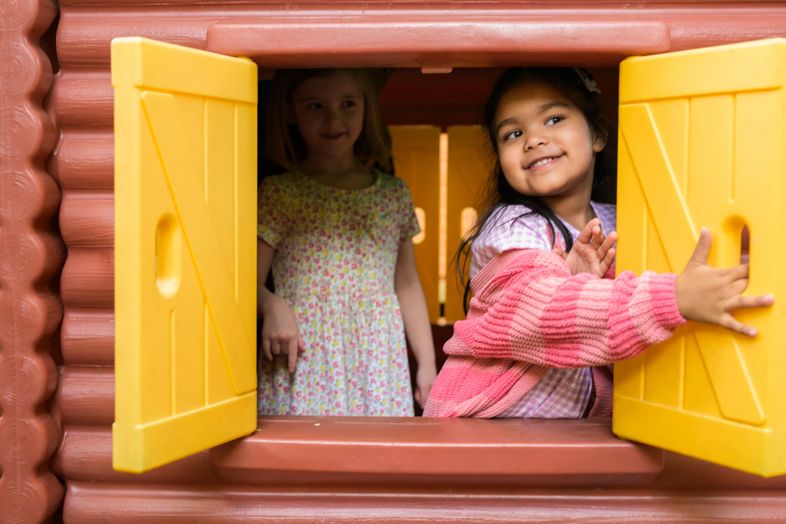 Two little girls in open window of play house